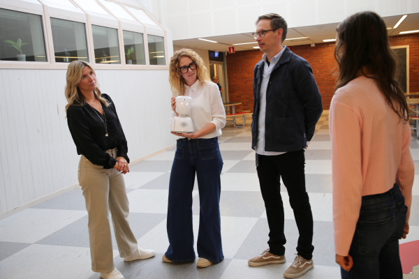 Tre personer samtalar med en elev i skolmiljö. en av dem håller upp skolroboten