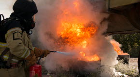 En elev med skyddskläder och brandsläckare, släcker en flammande eld.