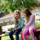Bilden föreställer två flickor som sitter på en bänk i Lögdö Bruk