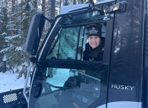 En kvinna sitter i en pistmaskin och tittar ut genom fönstret, tittar in i kameran och ler 