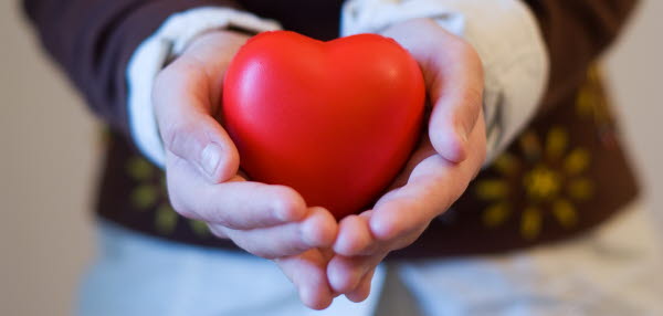 Bilden visar två händer som håller ett rött hjärta