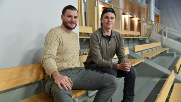 Två personer sitter på en läktare i en sporthall.