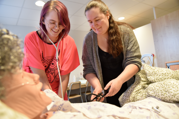 Marie Nilsén och Helena Rendahl arbetar med omvårdnadsdockan i metodrummet.