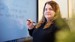 En kvinna står framför en digital whiteboard med en penna i handen.