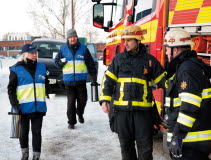 Två personer från Frivilliga resursgruppen bär på kaffetermosar. I bild syns även två brandmän bredvid en brandbil.