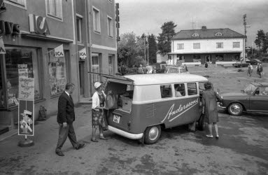 Svartvit bild som visar en gammal ICA-butik där folk lastar in varor bak på en buss i Timrå.
