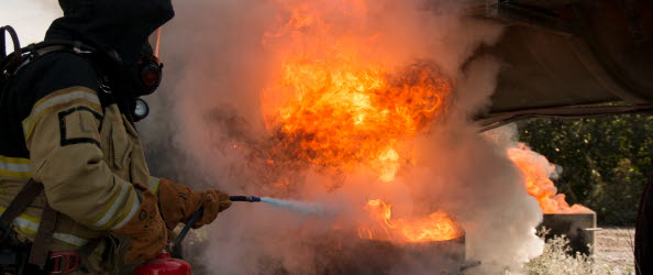 En elev med skyddskläder och brandsläckare, släcker en flammande eld.