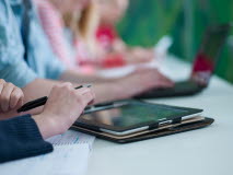Närbild på en grupp med studenter sitter vid ett skrivbord och arbetar vid laptops och en iPad