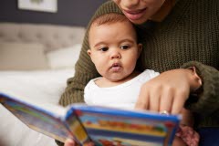 En liten bebis sitter i sin mammas knä och tittar i en färgglad bok