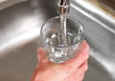 En hand håller ett glas under en rinnande vattenkran.