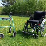 En rollator och en rullstol står på en gräsmatta.