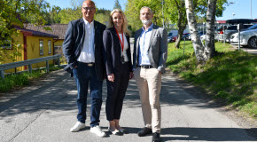 Tre personer står uppradade på en väg och tittar in i kameran.