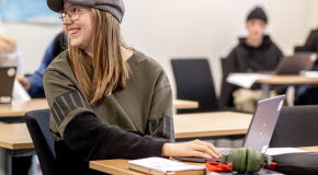 Elev som sitter vid en bänk i ett klassrum, ler och tittar bort.