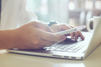 Bild på en person som använder en smartphone och en bärbar dator.