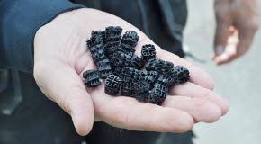 Ett femtontal svarta små platsbitar hålls i en öppen hand