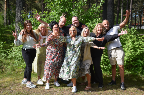 En grupp på nio personer står vänd mot kameran. De gestikulerar med armarna upp i luften.