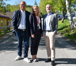 Tre personer står uppradade på en väg och tittar in i kameran.
