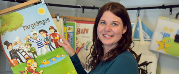 En kvinna håller upp en barnbok och tittar leendes in i kameran.