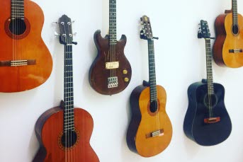Sex stycken gitarren hänger i olika höjder mot en vägg.