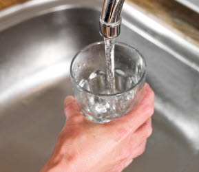 En hand håller ett glas vatten under en kran med rinnande vatten.