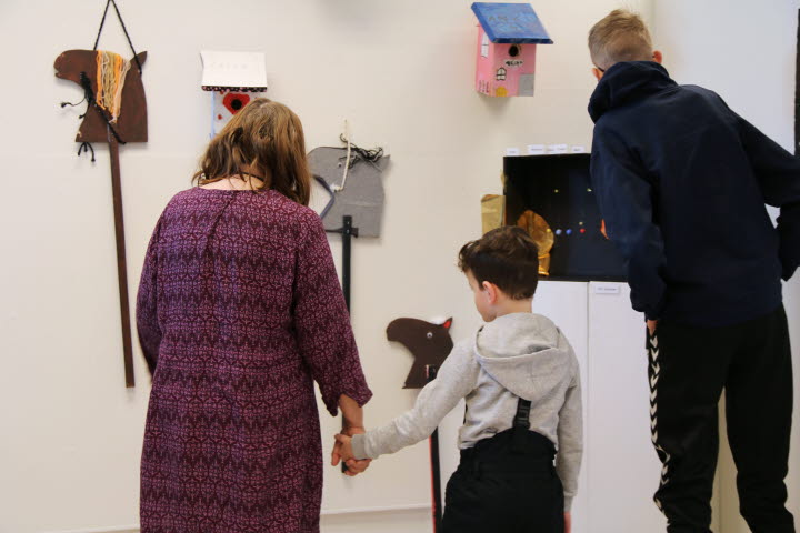 En vuxen och två barn tittar på olika konstverk som eleverna på grundsärskolan i Bergeforsen skapat