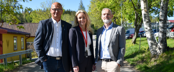 Tre personer står uppradade på en väg och tittar in i kameran.