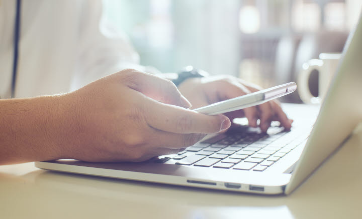 En person som håller i en telefon med en dator i bakgrunden