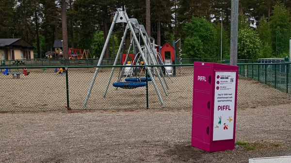 En rosa aktivitetsbox vid en lekpark.