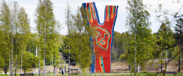 En bild över skulpturen Y:et vid Midlandaområdet. Runt omkring syns gröna träd, och i framgrunden skymtar man vatten.