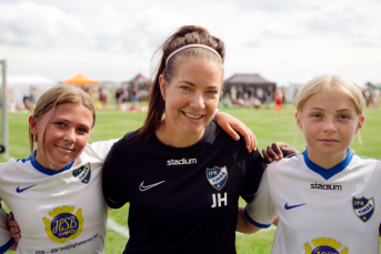 Tre tjejer står och håller om varandra på rad i fotbollskläder.