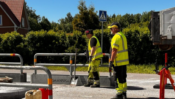 Två män i varselkläder står och jobbar vid ett övergångsställe.