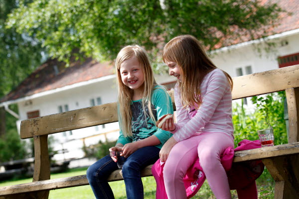 Bilden föreställer två flickor som sitter på en bänk i Lögdö Bruk