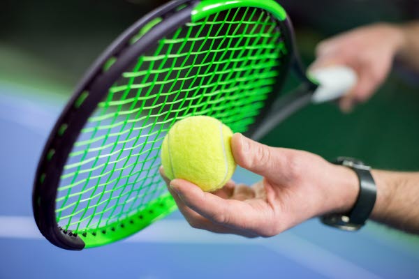 Bilden föreställer ett tennisrackert som en person håller i med ena handen och en boll i den andra.