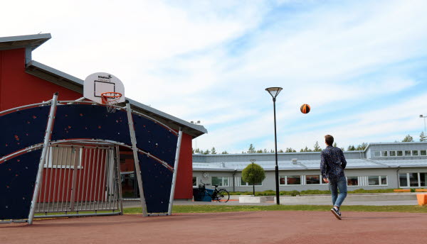 Bilden föreställer en pojke på en skolgård med en basketboll.