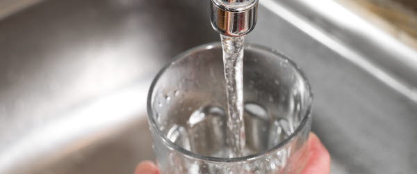 En hand håller ett glas vatten under en kran med rinnande vatten.