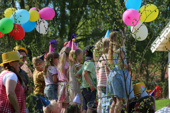 Barn från Böleängens förskola står på rad och sjunger låtar i det gröna gräset. Det är flera ballonger i olika färger i bilden.