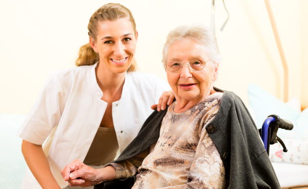 Bilden visar en vårdpersonal med en äldre kvinna i rullstol