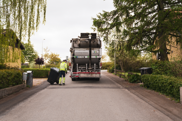 Chaufför tömmer en soptunna i en sopbil.