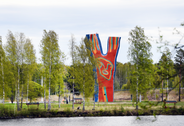 En bild över skulpturen Y:et vid Midlandaområdet. Runt omkring syns gröna träd, och i framgrunden skymtar man vatten.