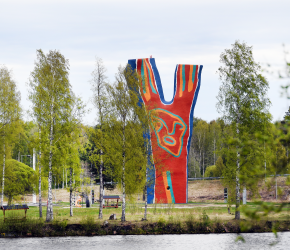 En bild över skulpturen Y:et vid Midlandaområdet. Runt omkring syns gröna träd, och i framgrunden skymtar man vatten.