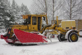 Bilden föreställer en traktor som är ute och plogar i snöfallet