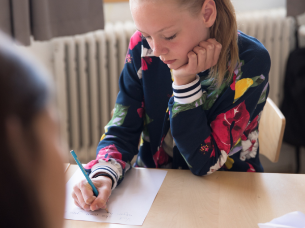 Ung kvinna sitter vid ett bord och skriver på ett vitt papper