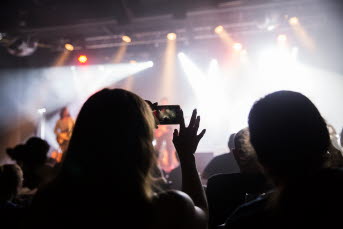En kvinna är på konsert och tar bilder med sin mobiltelefon.
