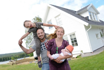 En familj står framför en vit trävilla.