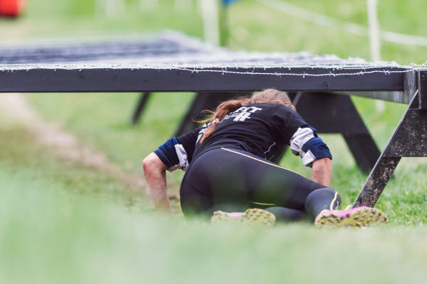 Bilden föreställer en kvinna som kryper under ett hinder vid Obstacle Race
