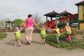 En förskolepedagog går hand i hand med 4 andra barn mot en lekpark.