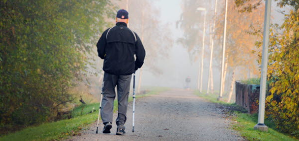 Bilden visar en man som går med stavar på en gångväg