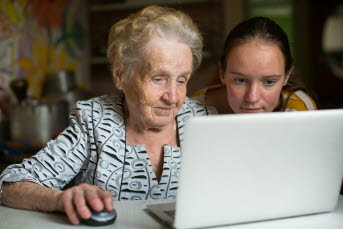 En äldre kvinna vid sin dator med en yngre tjej bredvid.
