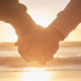 Två personer håller händerna på en strand i solnedgången.