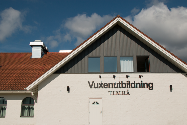 En vitt hus med brunt tak. Ovanför dörren på huset står det Vuxenutbildning Timrå.